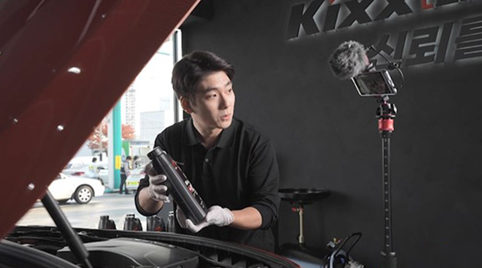 A Kixx Live mechanic performs an oil change while addressing the customer live via a camera mounted on a tripod