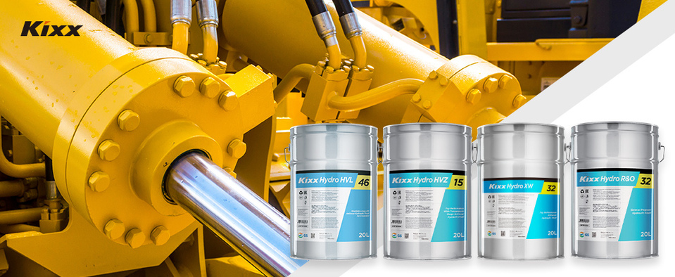 A shining yellow and chrome hydraulic system with three varieties of Kixx Hydraulic Fluid in the foreground in grey and blue drums. 