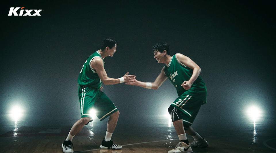 Minsu and Hyunsoo, dressed in green and white Kixx basketball gear, celebrate their win by high-fiving against a dark backdrop.