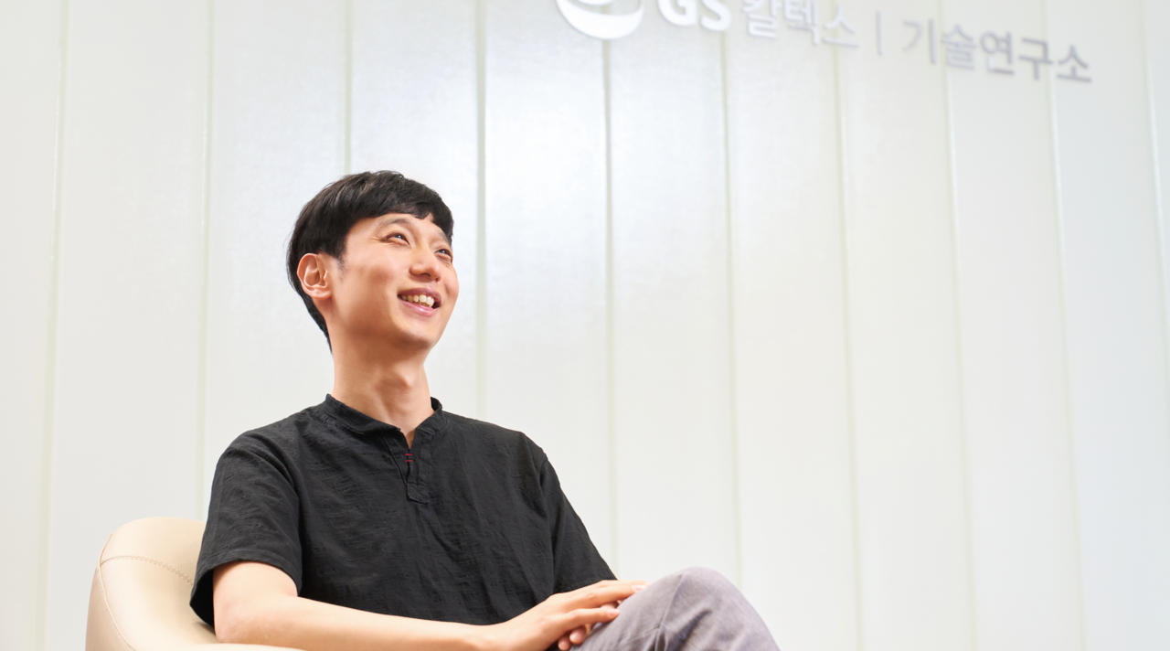 A smiling Rae Wook Cho sits in front of GS Caltex R&D Center signage and looks off-camera