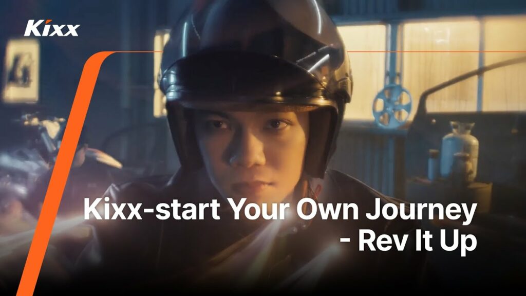 Scene from a Kixx commercial featuring a motorcycle rider in a helmet with the tagline ‘Kixx-start Your Own Journey – Rev It Up’ displayed on screen.