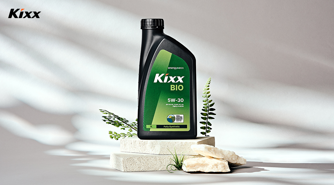 A bottle of Kixx BIO sits on stones in front of a white backdrop with shadows falling across it. 