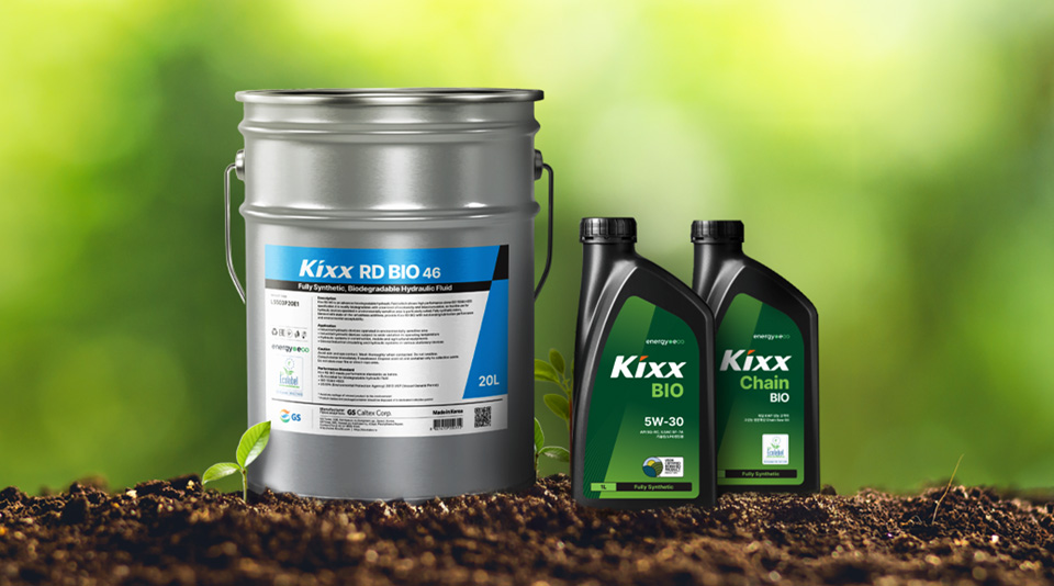 Биосмазочные материалы Kixx, размещённые на почве на фоне зелёной листвы, включая большую металлическую бочку и бутылки моторного м